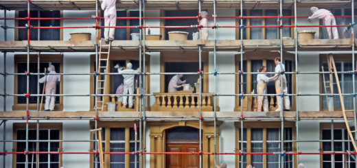 Scaffolding surrounding a big house with people painting it
